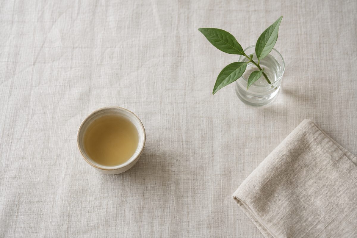 A cup of pale tea, a green sprig and a folded cloth